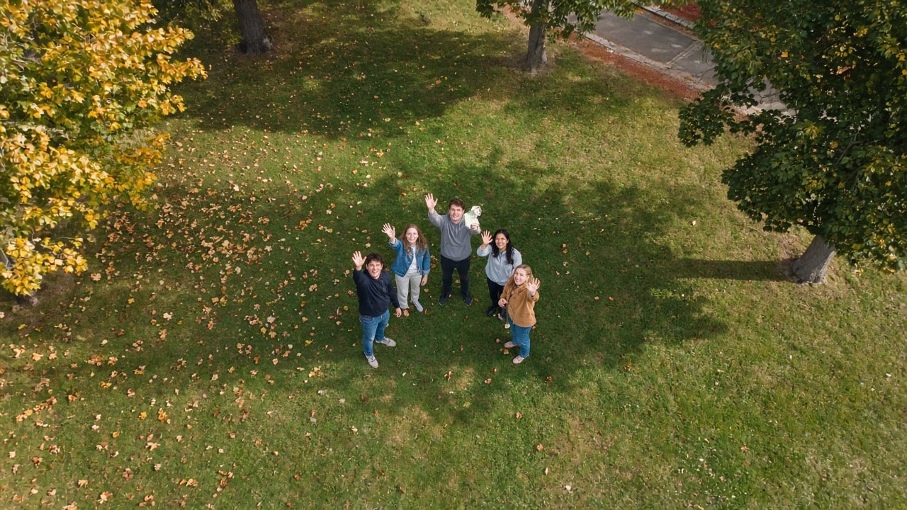Students on a campus lawn waving up at the drone after a cash drop